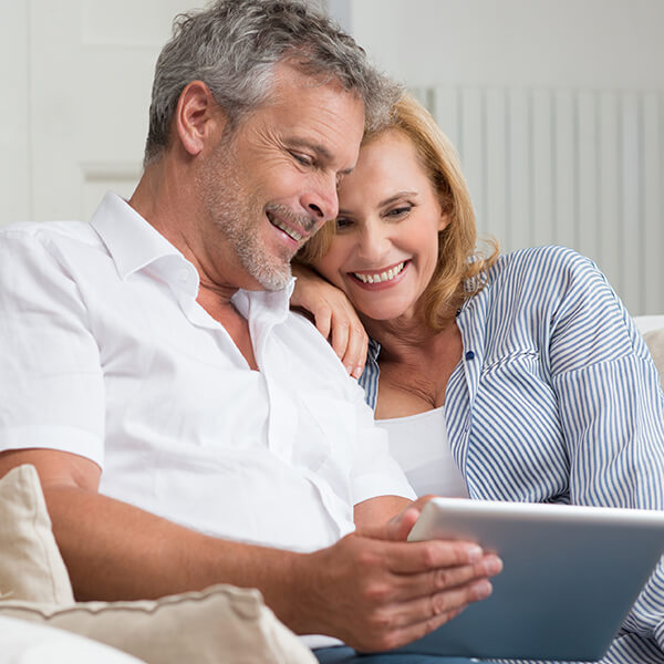  A Couple in their 50s enjoying their time while sitting on the couch browsing a tablet. 