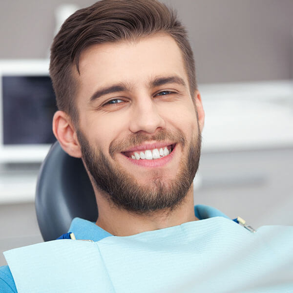A smiling man is sitting on a dental chair wearing a dental bib