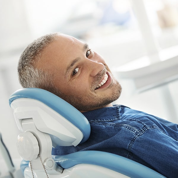 A man lying in a dental chair while showing his white teeth