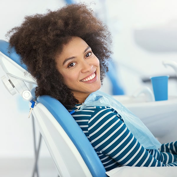 A young woman smiling and sitting in a dental chair while wearing a dental bib