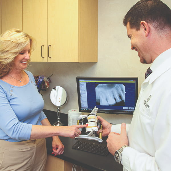 A smiling male dentist is discussing a dental procedure with a lady patient