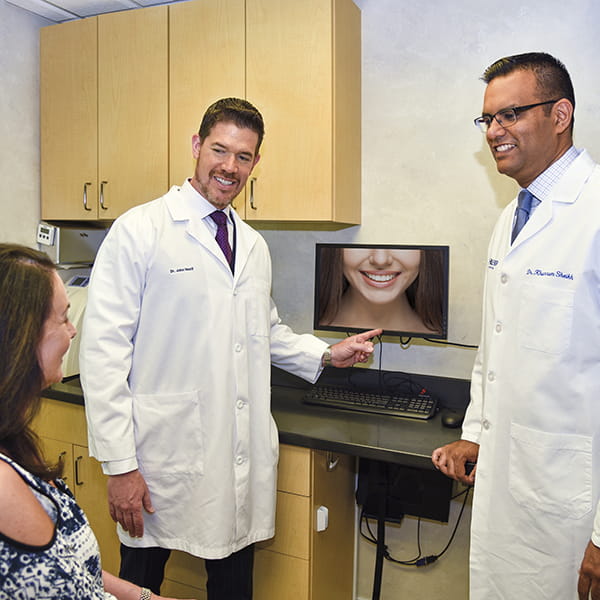 Two male dentists presenting a picture of a bright white smile to a lady patient who is sitting in front of them 