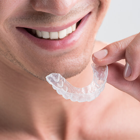  A smiling person is holding an Invisalign with his left hand