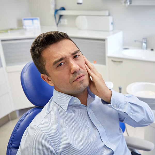 A man sitting on a dental chair is in pain and holding his left cheek