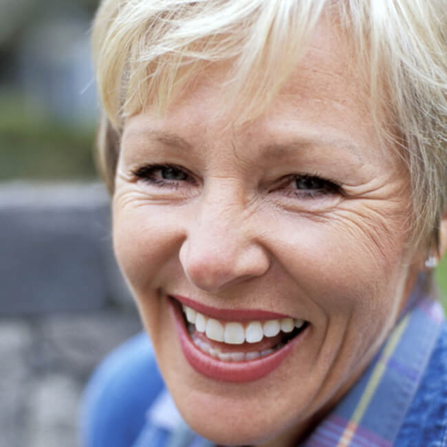  An old woman with white teeth and blonde hair smiling and wearing a sweater