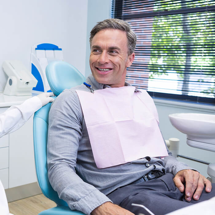  A man on a dental chair wand wearing a dental bib is looking at his right
