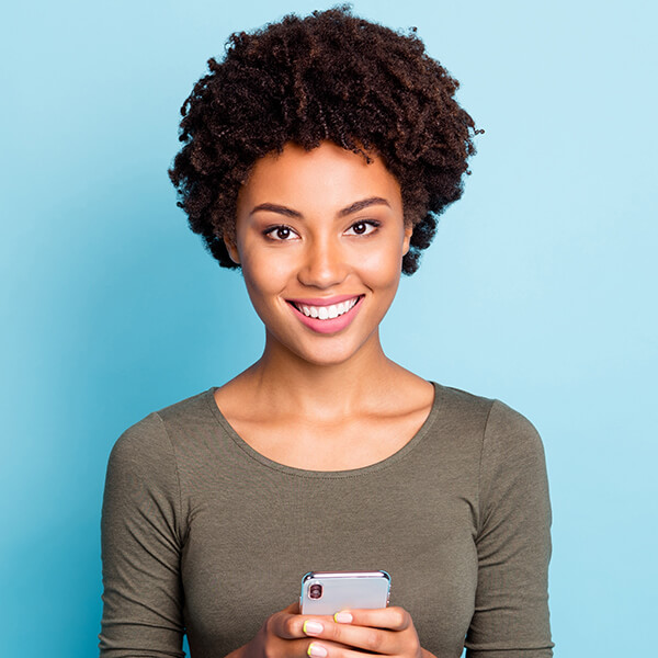 a black woman with a curly wavy hair wearing a round neck shirt holding her phone  Giving a big smile 