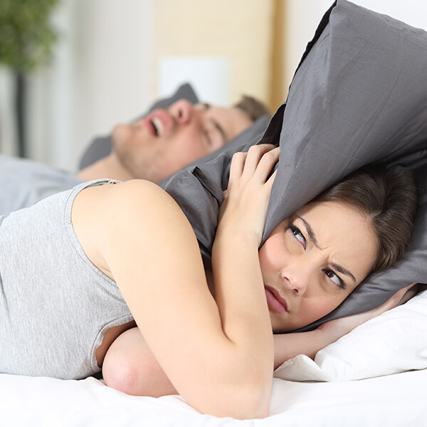 a wife covers her ears with a pillow while husband is asleep 