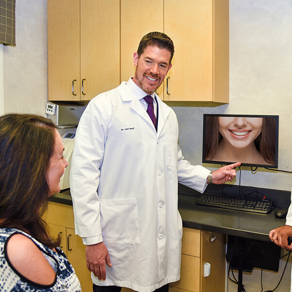 Two male dentists presenting a picture of a bright white smile to a lady patient who is sitting in front of them 